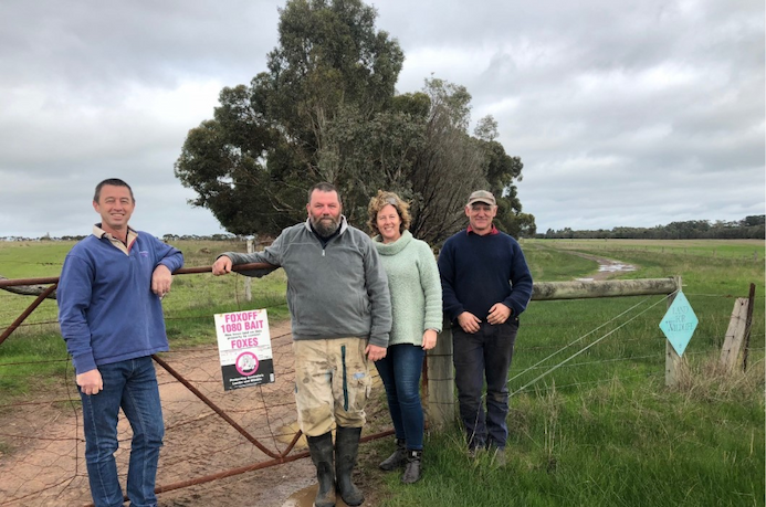 Four people posing in front of a fence on a farm.