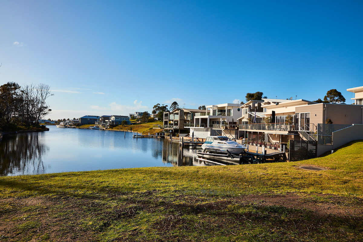 An image of the Gippsland Lakes showing a flat body of water with houses and docks in the background on a sunny day  