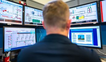 A man in front of a bank of computers monitoring data