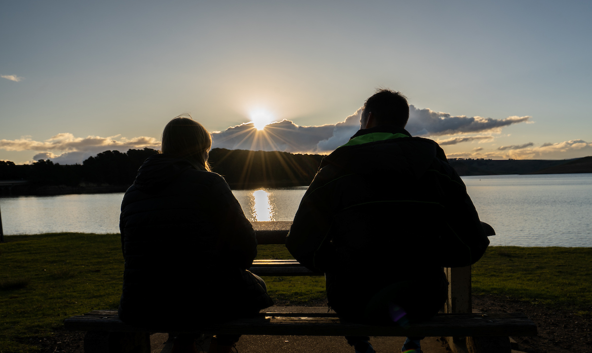 Two people in shadow looking at a reservoir  