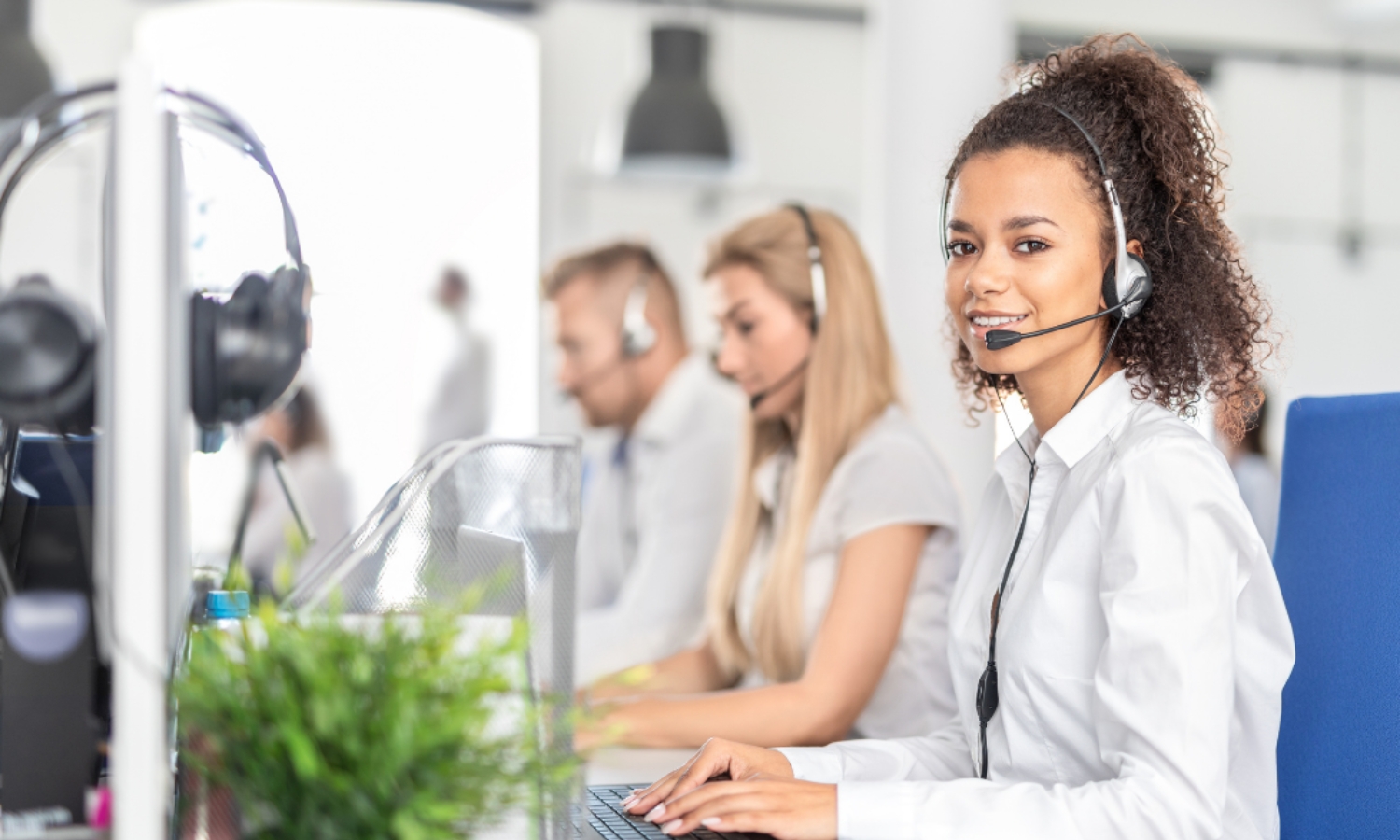 Primary Campaign - help paying your bills Person wearing headset and a white shirt sits at a desk with hands on keyboard in an office setting