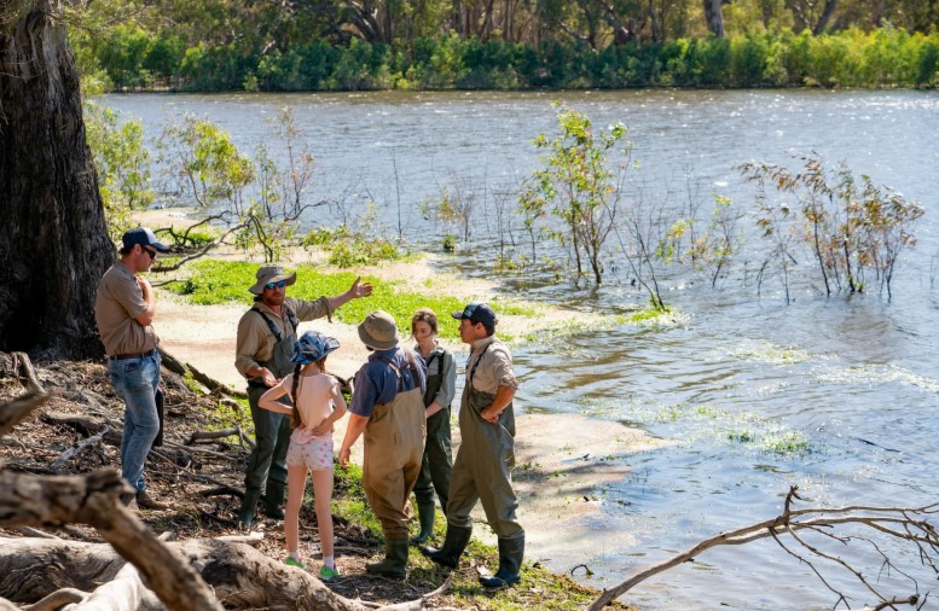 A group of people wearing waterproof overalls stand on the edge of a river. Image credit Mallee CMA.