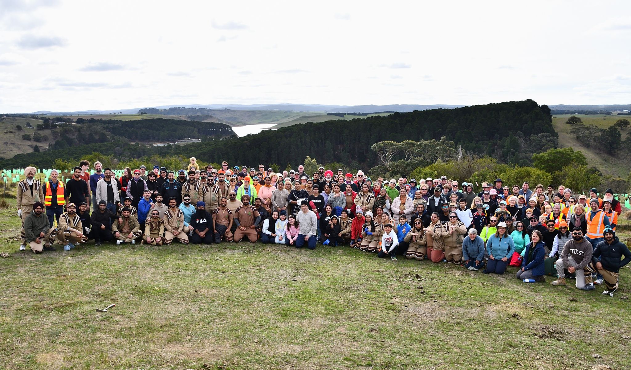 A very large group of people pose for a photo in an open grassy area with hills in the background.